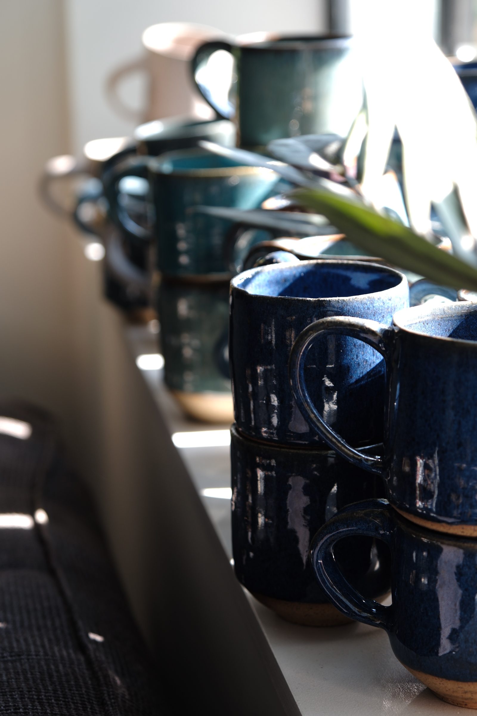 Stacks of blue glazed handmade mugs in golden light